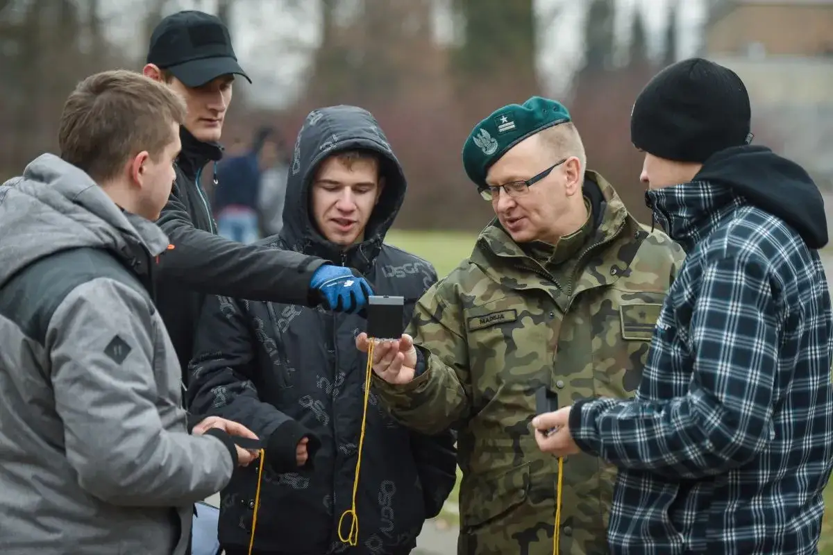Żołnierz w zielonym berencie pokazuje młodym ludziom kompas podczas szkolenia podstawowego wojsko.