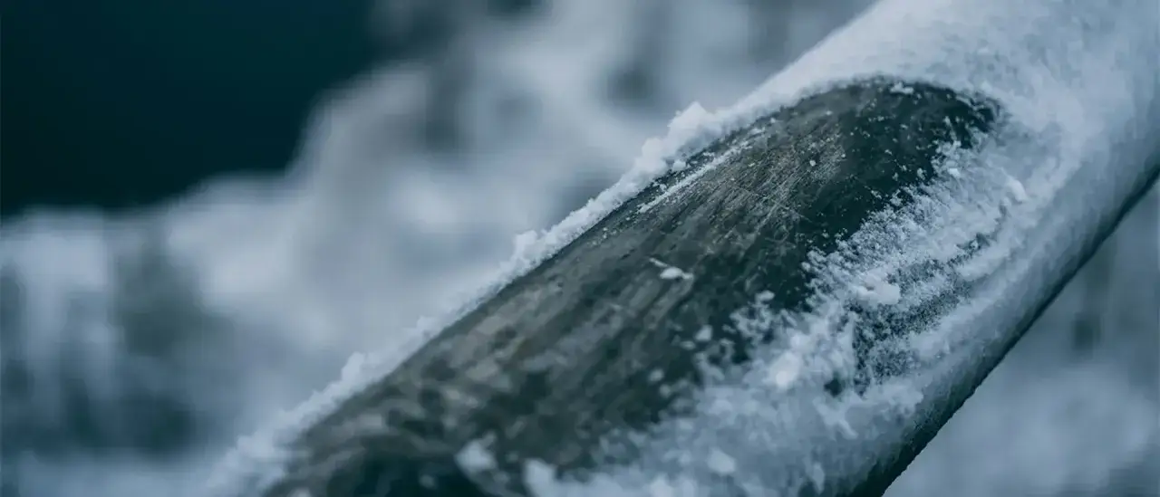 En närbild av frusna vattenledningar i marken, täckta av snö. Vattnet har frusit till is.