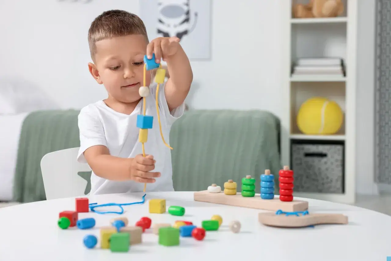 Kleiner Junge fädelt bunte Holzperlen auf, ein spielerischer Ansatz für Ergotherapie mit Kindern.