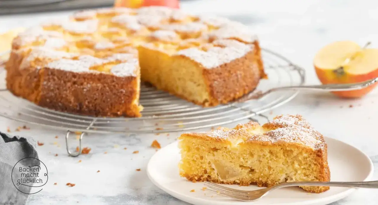 Ein saftiger, glutenfreier Kuchen mit &Auml;pfeln, best&auml;ubt mit Puderzucker. Ein St&uuml;ck auf einem Teller mit einer Gabel daneben.