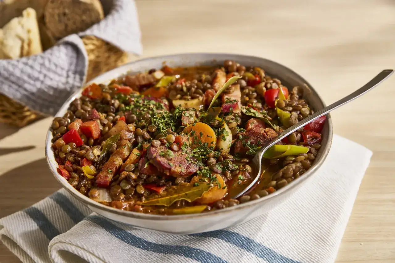 Un plato humeante de lentejas estofadas con verduras y chorizo, la auténtica lentejas receta de la abuela, servido en un cuenco rústico.
