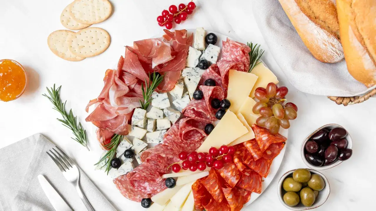 Un ricco piatto di antipasti di terra: salumi, formaggi, olive, uva e crostini, perfetto per un aperitivo.