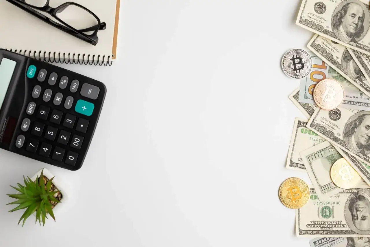 Kalkulator, okulary, notatnik i monety bitcoin obok dolarów. Obrazek sugeruje analizę finansową, kluczową dla ustalenia podstawy wymiaru składek na ubezpieczenie zdrowotne.