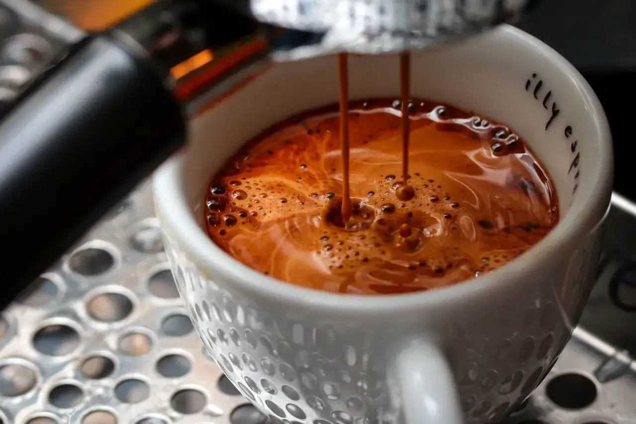 En kopp med americano kaffe fylls p&aring; fr&aring;n en espressomaskin. Kaffet har en fin crema och sm&aring; bubblor.