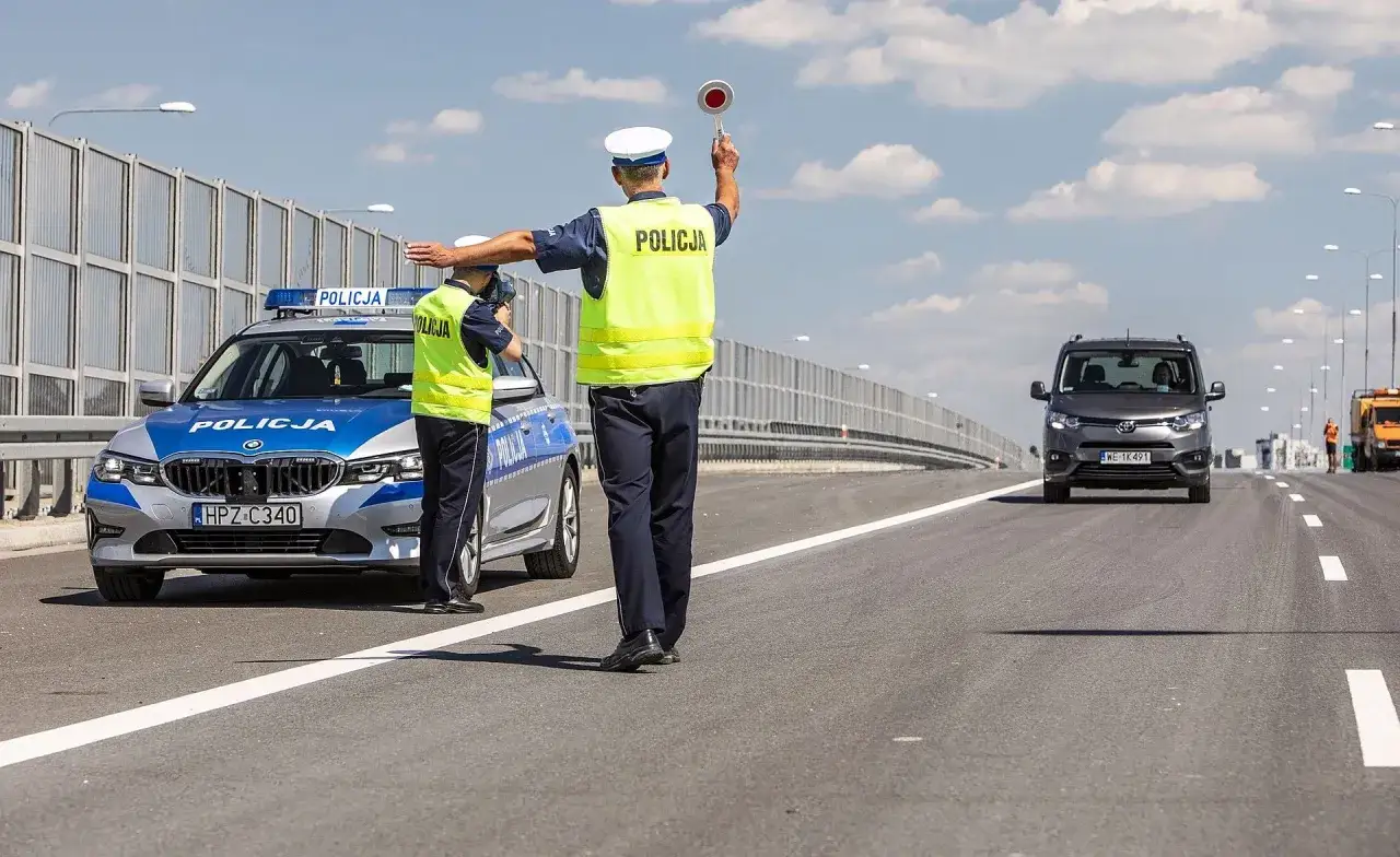 Policjanci kontrolują ruch na drodze, sprawdzając dopuszczalną masę całkowitą pojazdów. Jeden z nich kieruje ruchem, drugi mierzy prędkość.