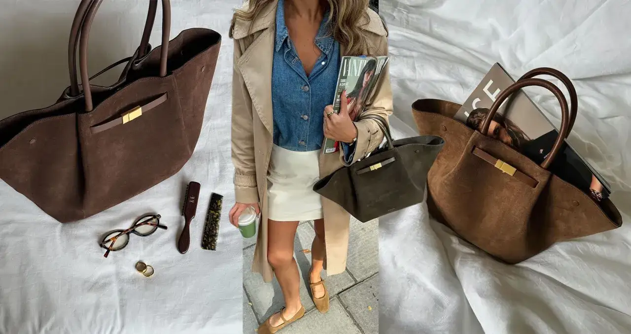 Braune Wildleder Demellier New York Tote mit goldenem Verschluss, daneben Brille, Ringe und Bürsten.