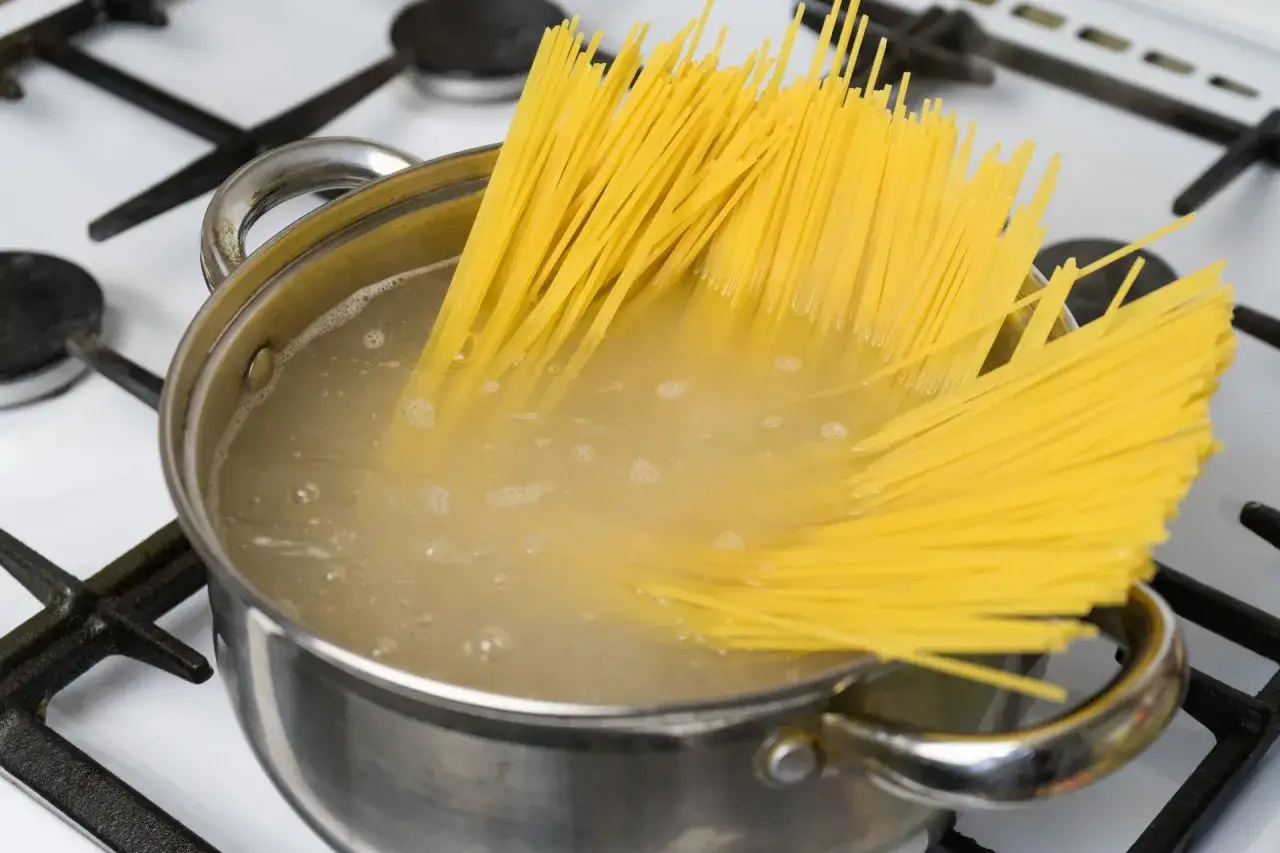 Długie, ż&oacute;łte nitki spaghetti gotują się w garnku, tworząc idealny makaron al dente.