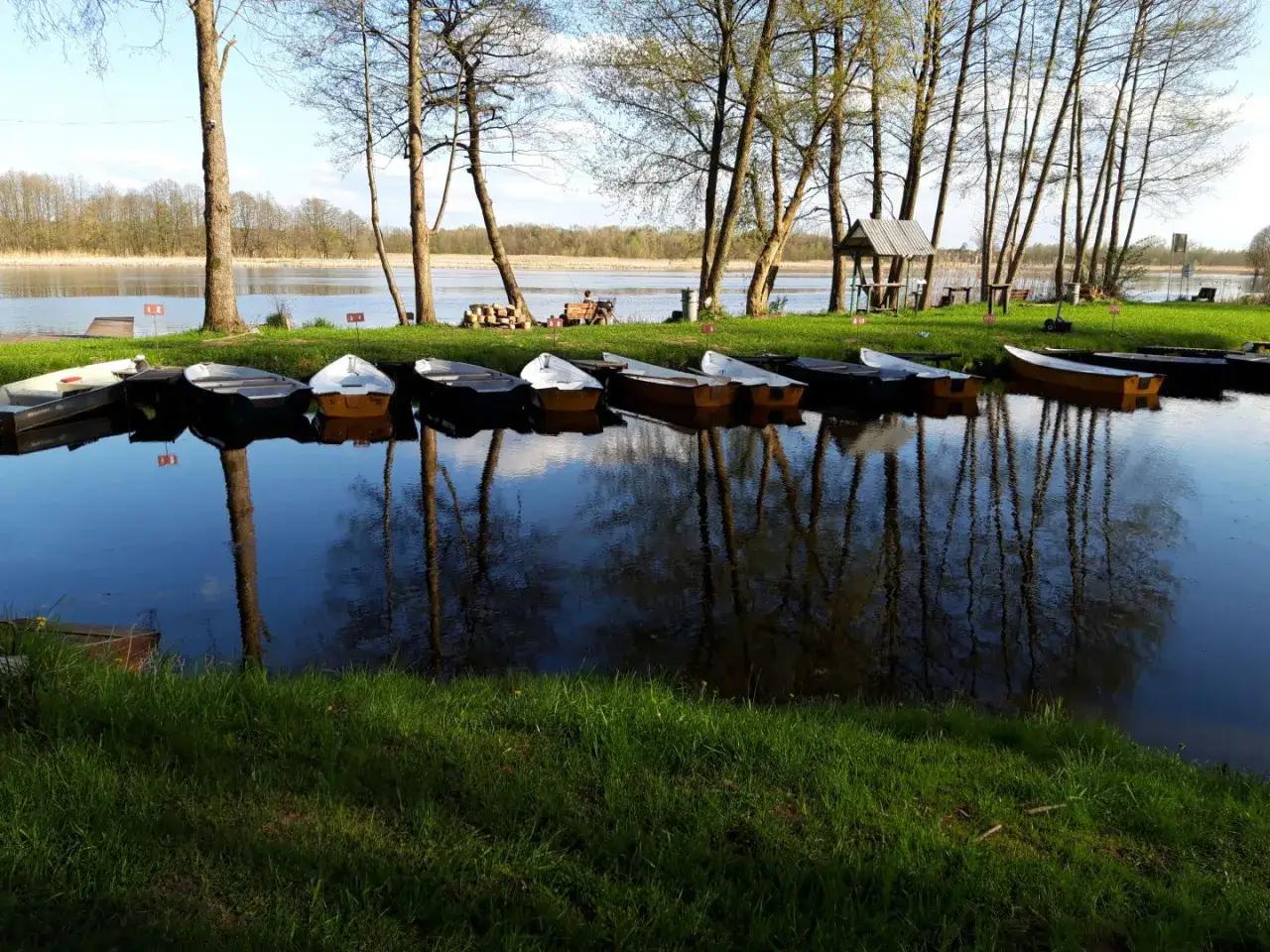 Rząd łodzi czeka nad spokojnymi stawami w piaskach, odbijając się w tafli wody.