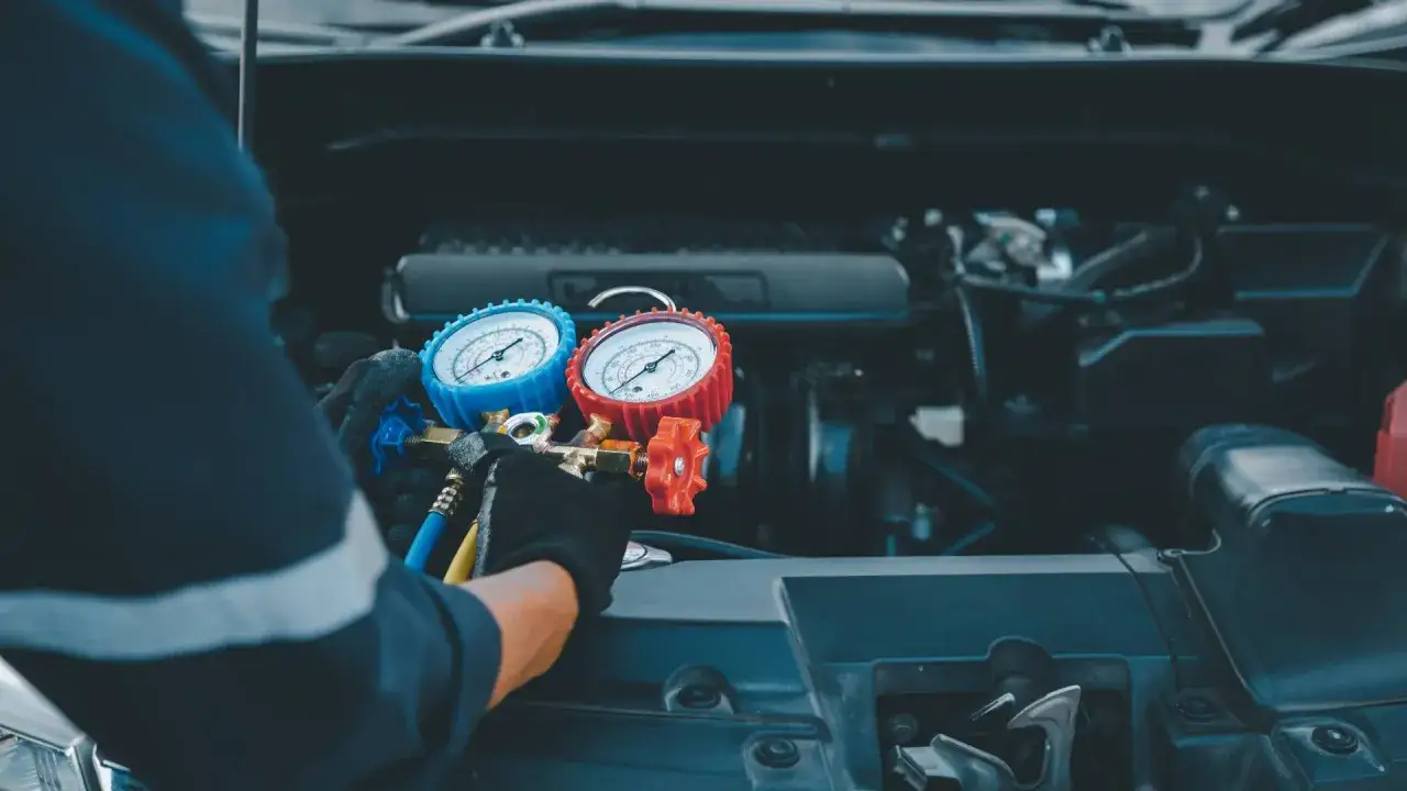 Tecnico con guanti effettua il ricaricare aria condizionata auto, usando un manometro per controllare il gas.