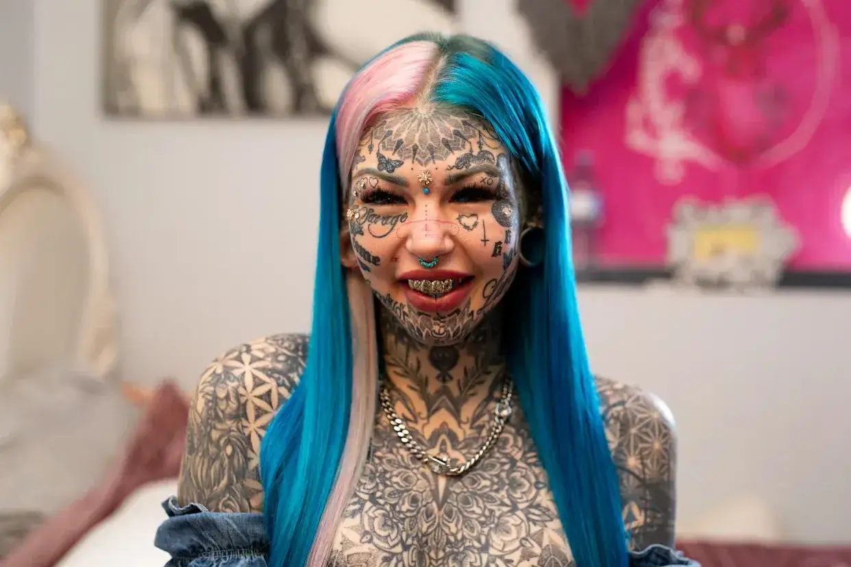 Eva Tiamat Medusa, z twarzą pokrytą tatuażami, niebiesko-różowymi włosami i złotymi zębami, emanuje siłą.