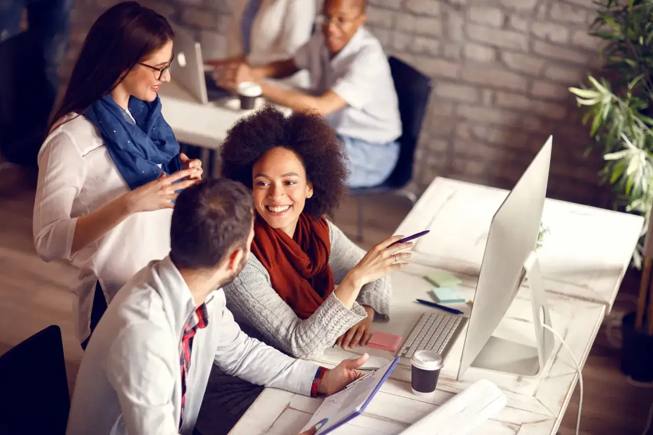 A diverse team collaborates, showcasing employee engagement and leadership. They discuss a project, smiling and pointing at a computer screen.