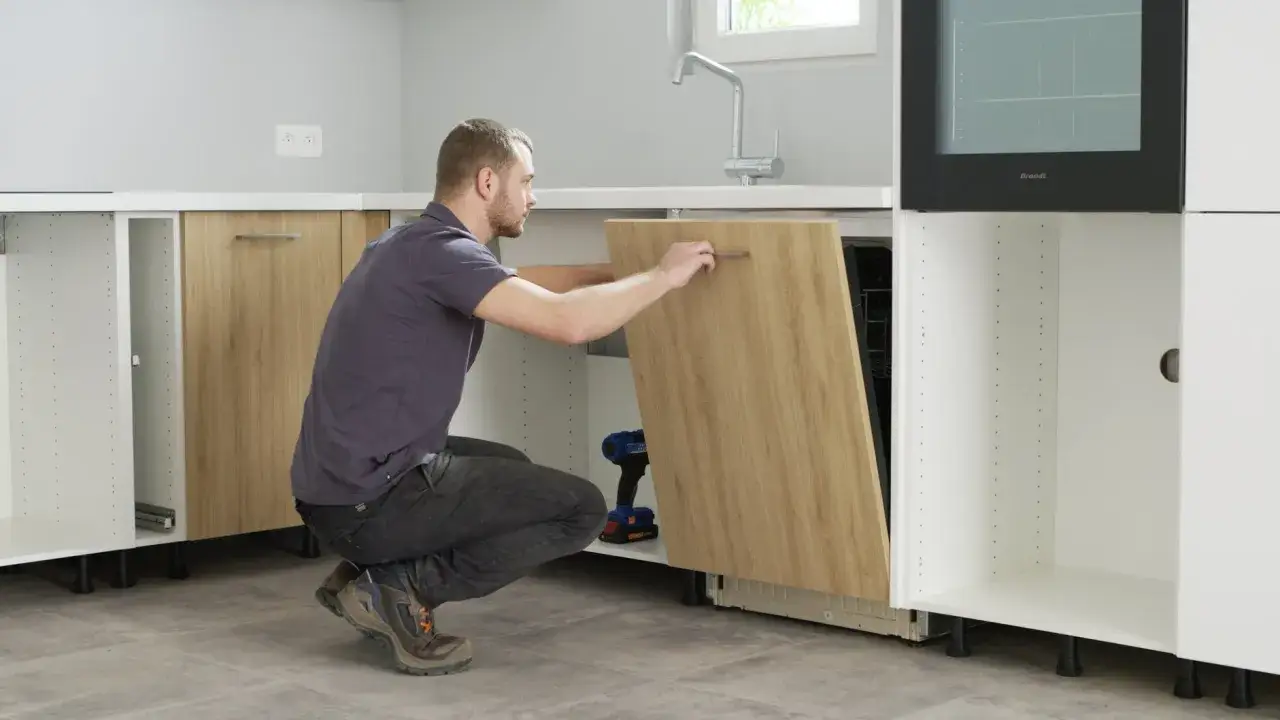 Uomo che esegue il montaggio lavastoviglie incasso, posizionando il pannello frontale in legno.