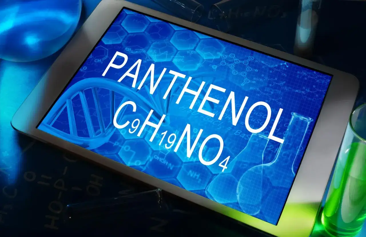 Tablet z napisem PANTHENOL C9H19NO4 na tle wzorów chemicznych i helisy DNA. Obok probówki z zielonym płynem.