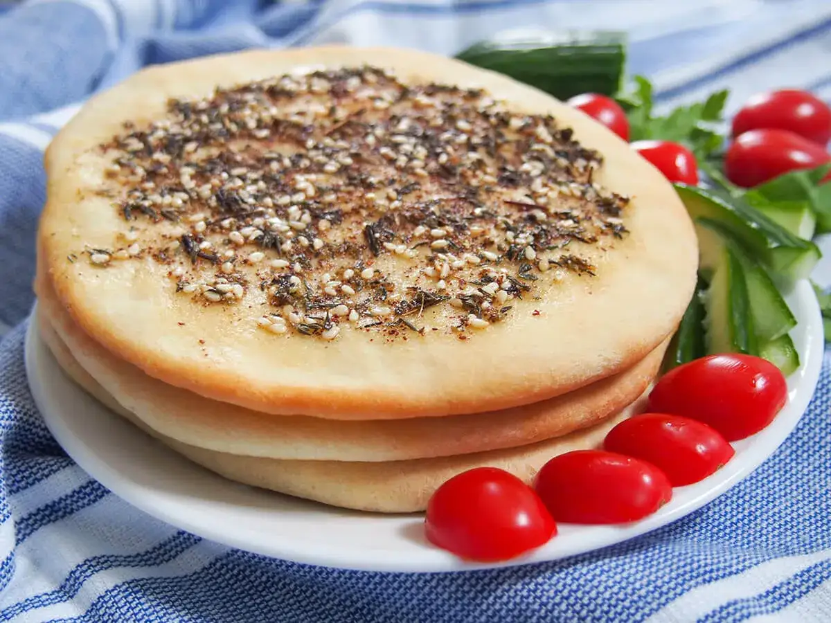 En stapel manakish med za'atar och sesamfr&ouml;n, serverad med k&ouml;rsb&auml;rstomater och gurka. Ett enkelt manakish recept.