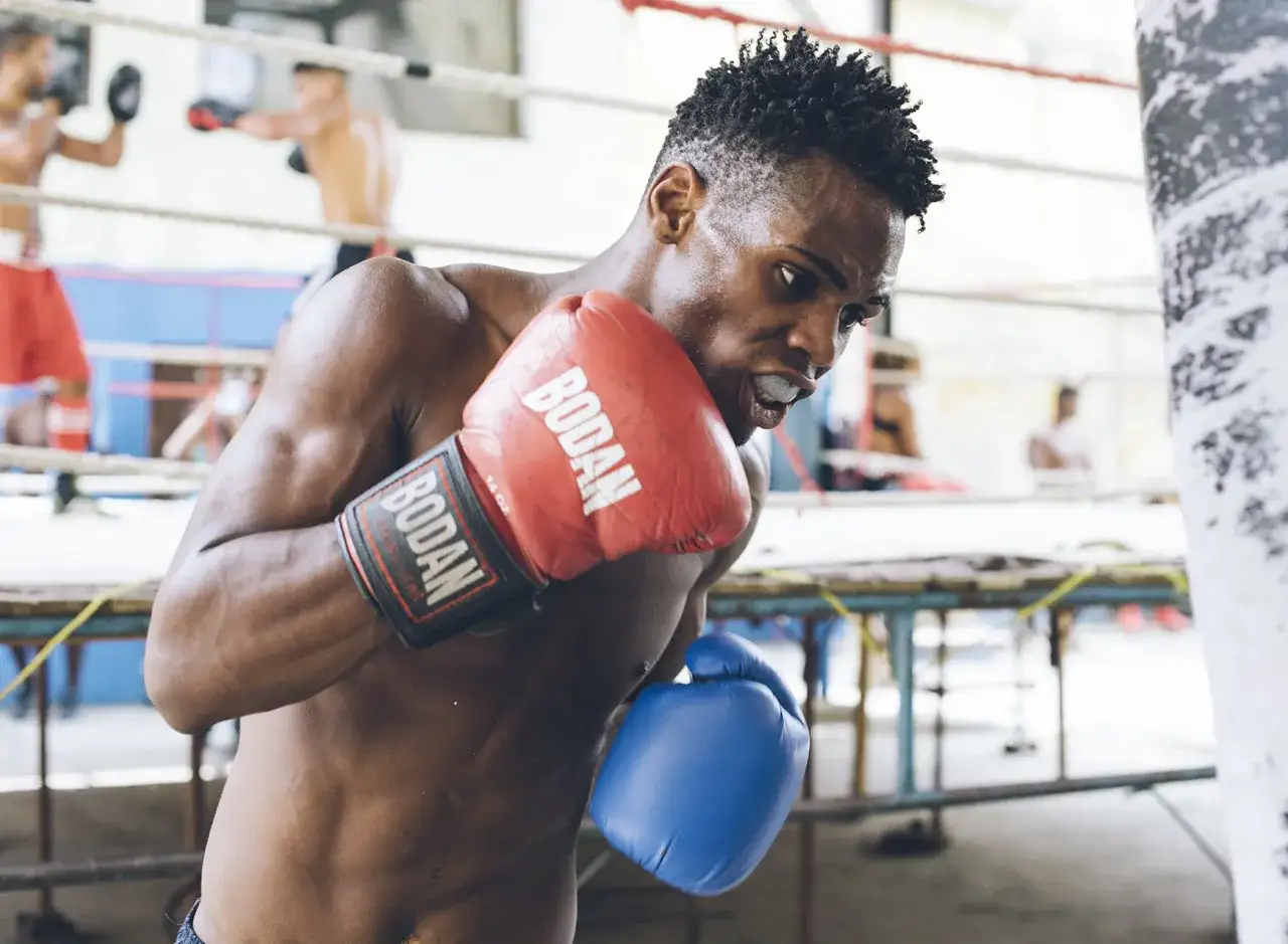 A determined cuban boxer in the USA trains intensely in a boxing ring, sweat glistening on his skin as he throws a punch.