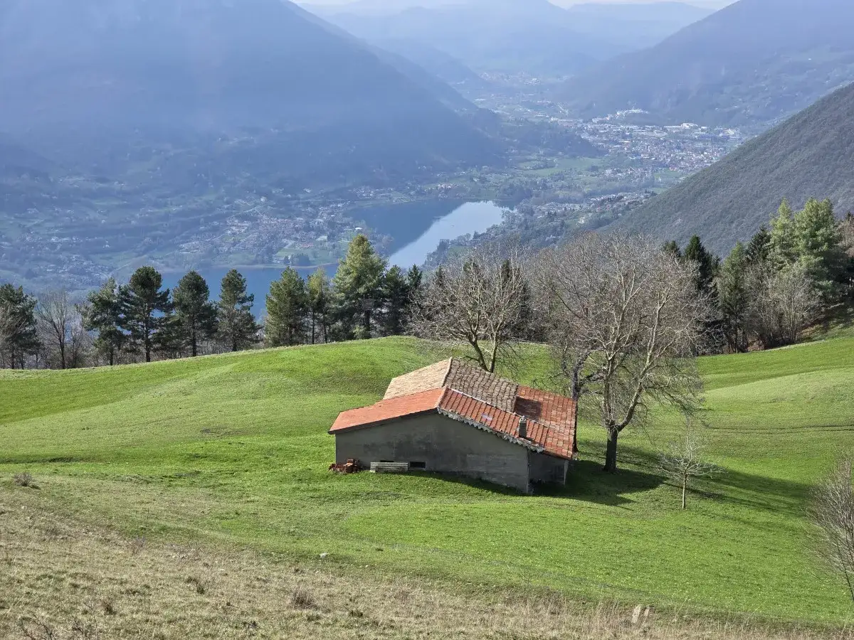 Un casolare con tetto rosso su un prato verde, con il lago di Endine e le montagne sullo sfondo.