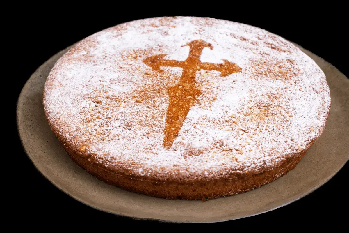 Pastel redondo espolvoreado con azúcar glas, con una cruz de Santiago en el centro. Un delicioso ejemplo de reposteria y pasteleria.