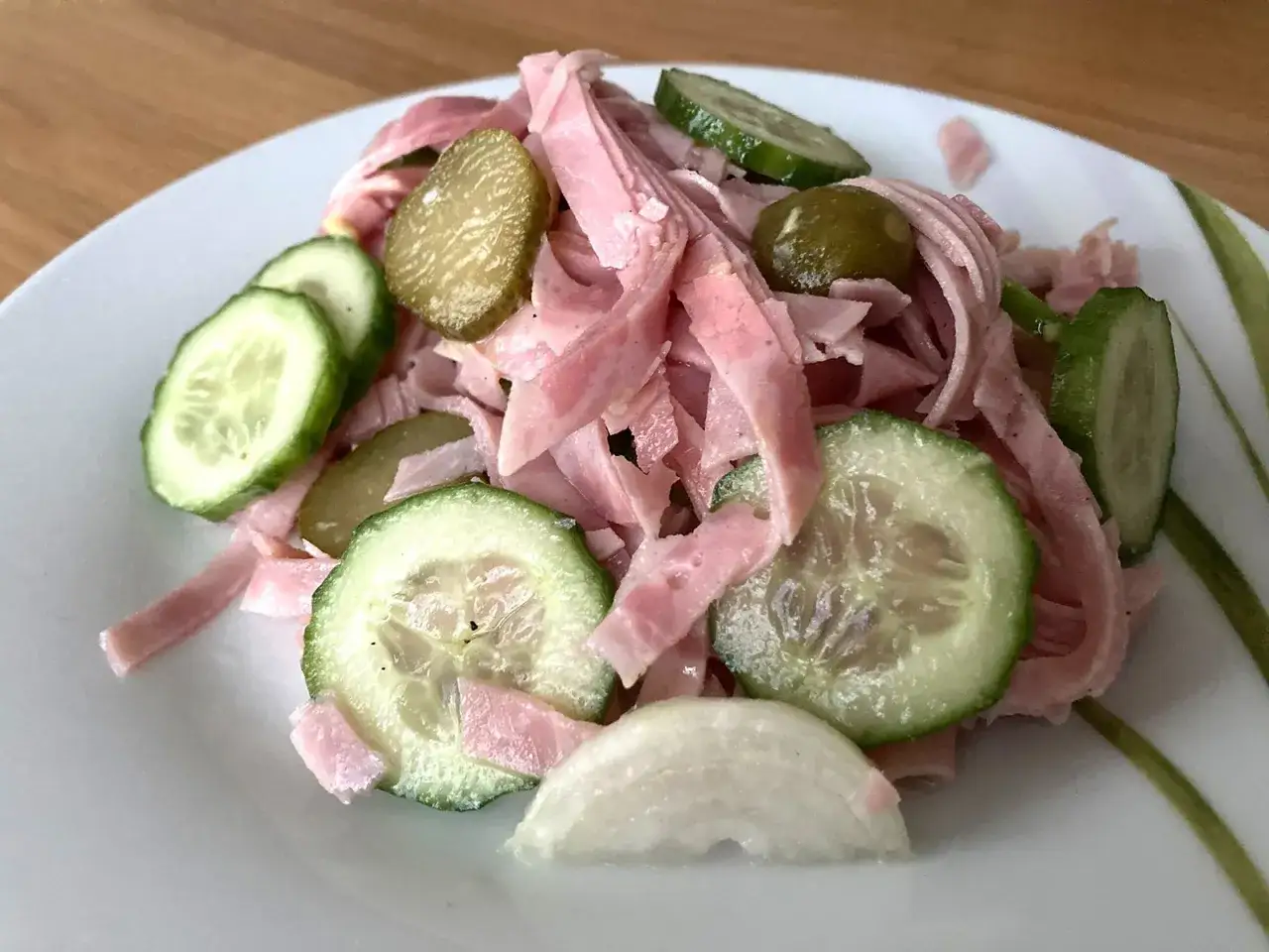 Ein leckeres Fleischsalat Rezept mit Gurkenscheiben und Zwiebeln auf einem Teller.