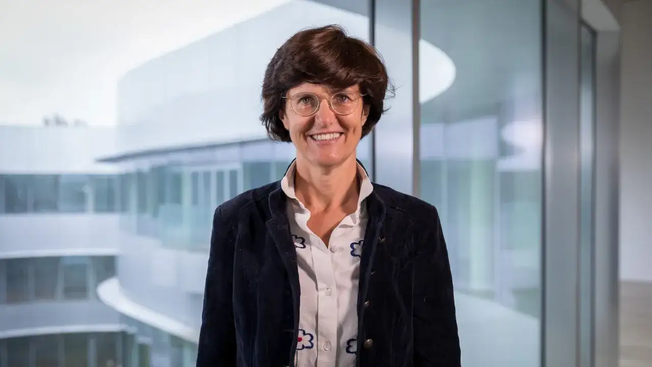 Paola Dubini, sorridente, indossa una giacca blu scuro e una camicia bianca con fiori.