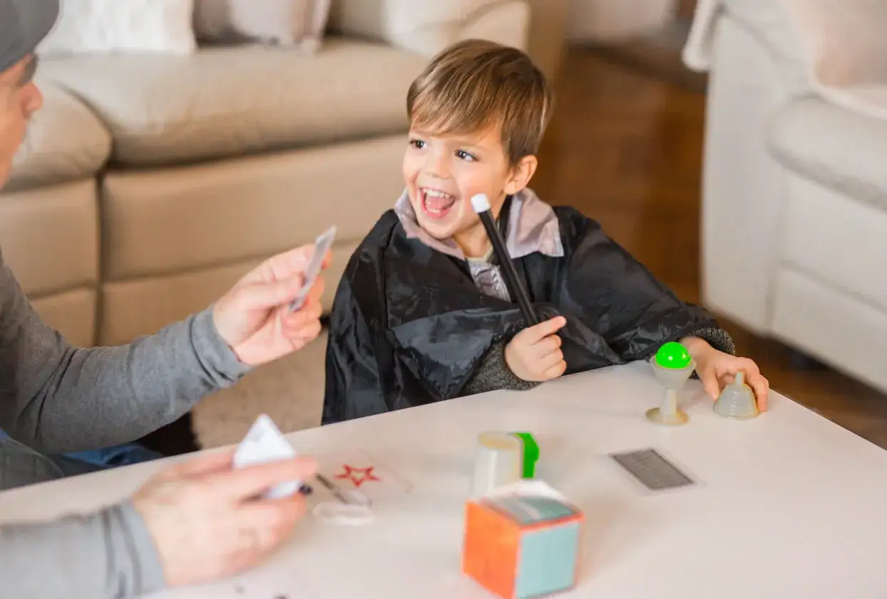 Niño con túnica de mago practica trucos de magia para hacer en casa, con varita y cartas.