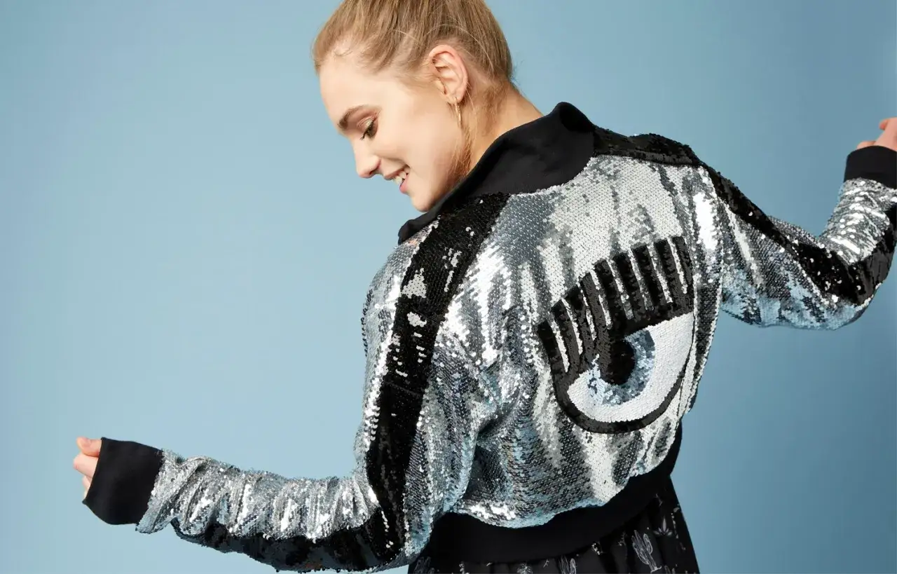 Uśmiechnięta Chiara Ferragni w błyszczącej kurtce z cekinami i motywem oka.