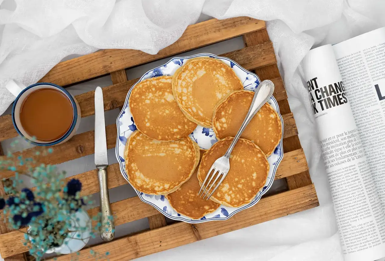 Recette pancakes fluffy : des pancakes dor&eacute;s et moelleux sur une assiette d&eacute;cor&eacute;e, accompagn&eacute;s d'une tasse de caf&eacute; et d'un journal.