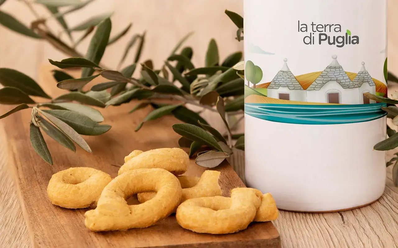 Taralli pugliesi su tagliere di legno, accanto a un contenitore con il logo 