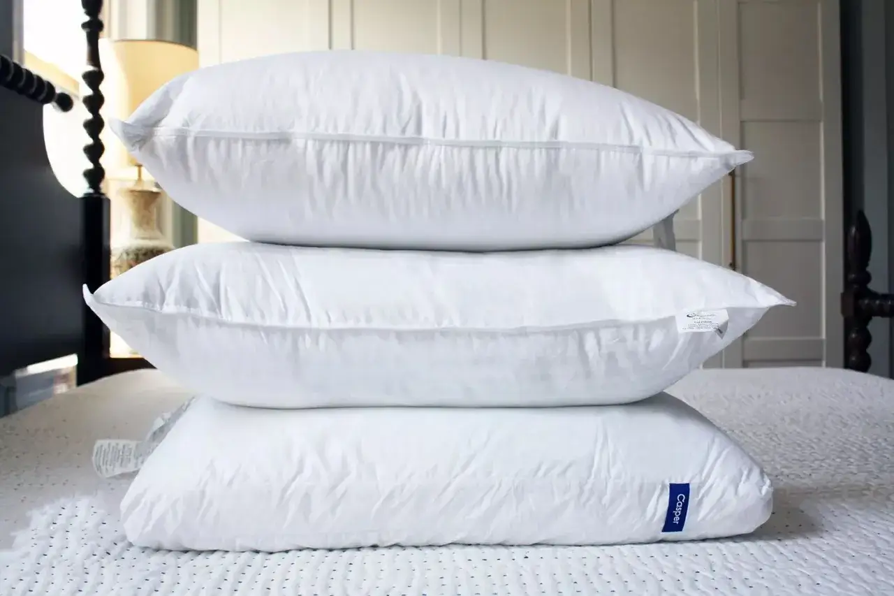 A stack of three white pillows, showcasing different types of pillows for a comfortable sleep.
