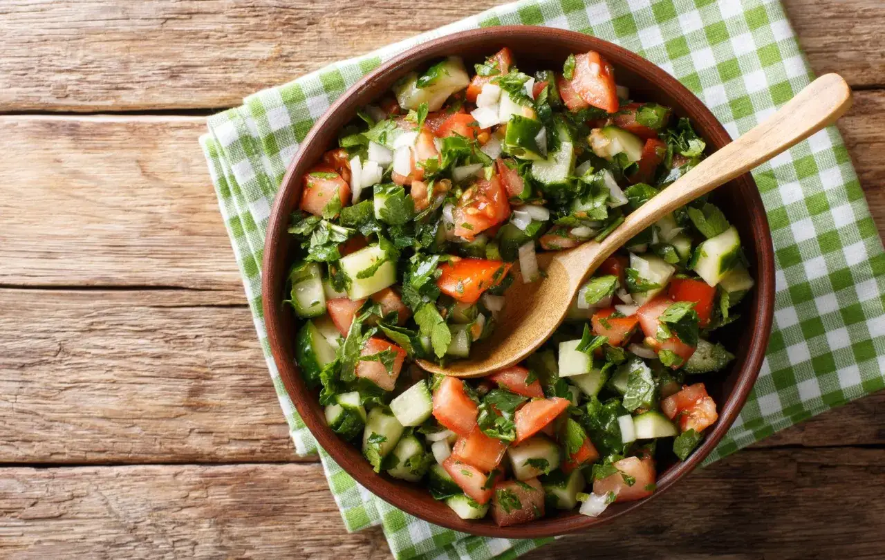 Una fresca insalata di cetrioli, pomodori e prezzemolo in una ciotola di terracotta, pronta per essere gustata.