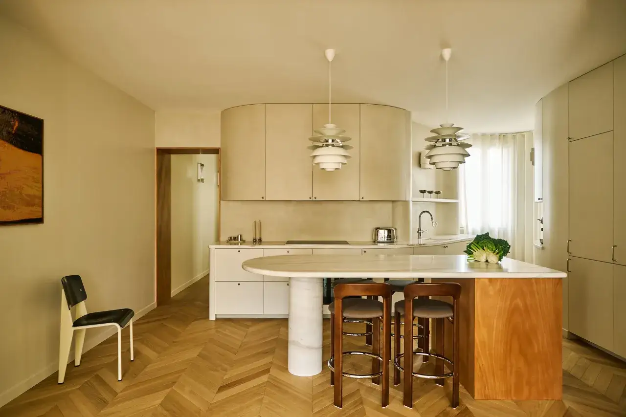 Elegantes cocinas modernas con isla de mármol, taburetes de madera y lámparas colgantes esculturales.
