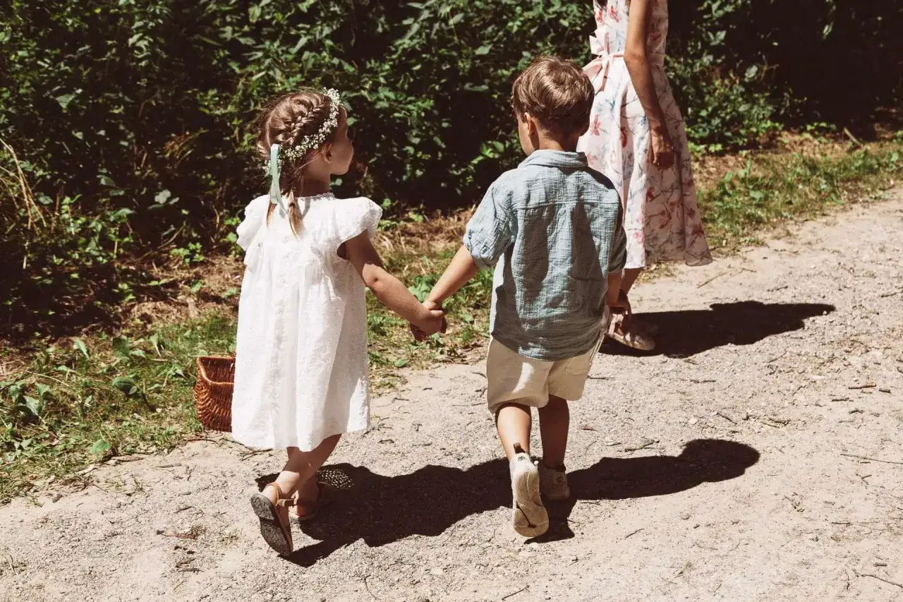Zwei Kinder, ein M&auml;dchen mit Blumenkranz und ein Junge, halten H&auml;ndchen auf dem Weg zu einer Hochzeit mit Kindern.