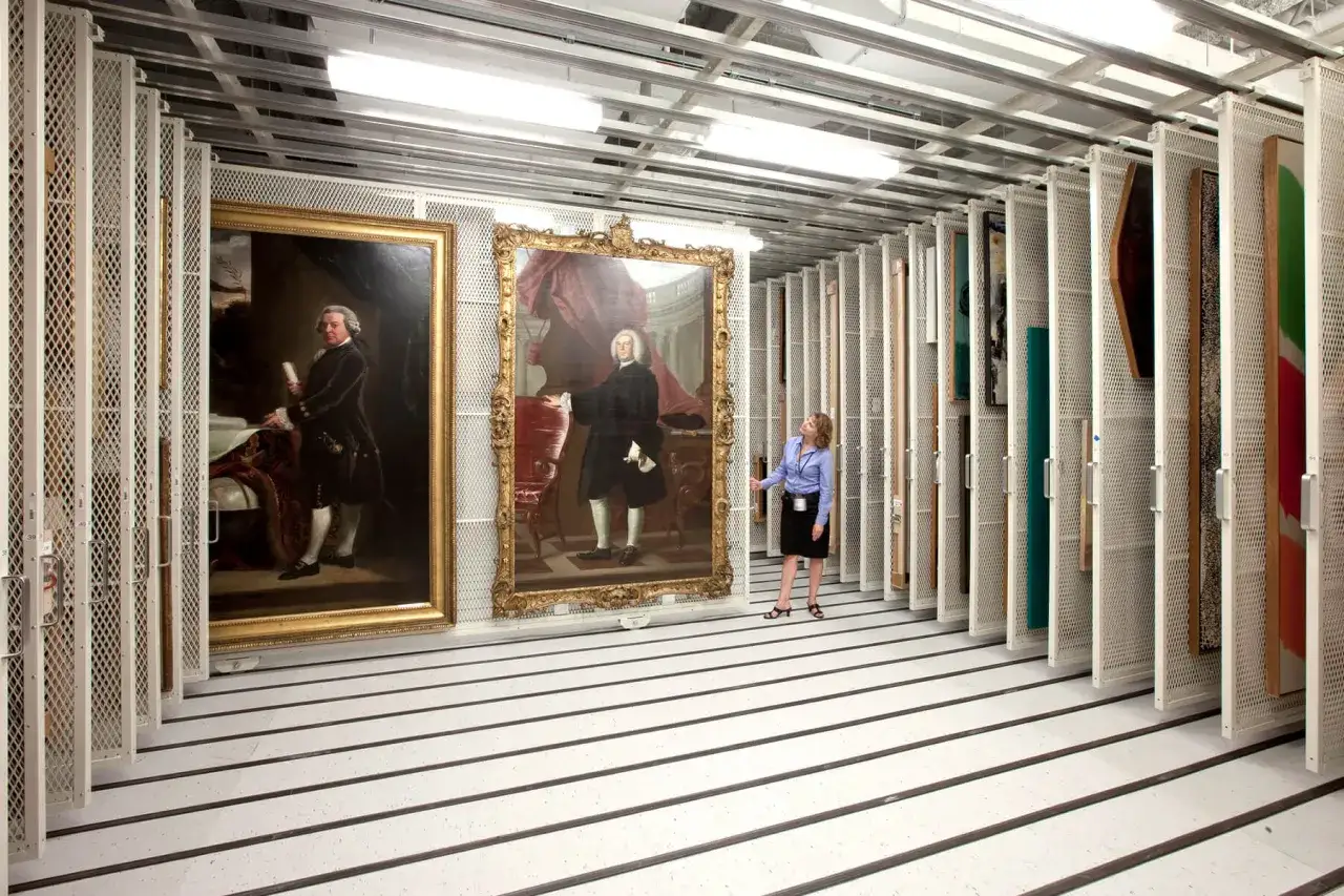 A curator examines portraits in a museum storage facility.