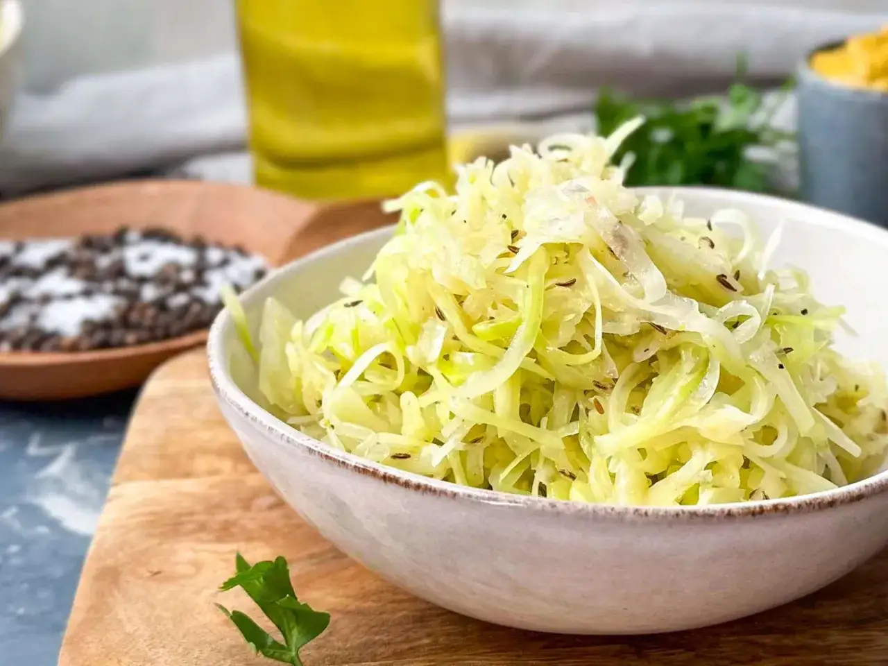 Frischer Krautsalat, wie im originalen Rezept Coleslaw, in einer Schüssel. Daneben Gewürze und Öl.