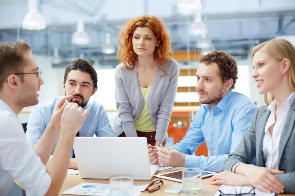 Teamwork: Fünf Kollegen besprechen Ideen, um die **Kommunikation verbessern** zu können. Ein Laptop und Dokumente liegen auf dem Tisch.