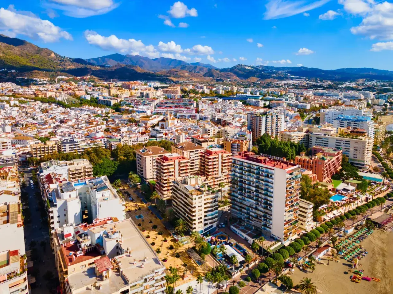 Widok z lotu ptaka na nadmorskie miasto Marbella, z górami w tle. Widać plażę, hotele i budynki mieszkalne.