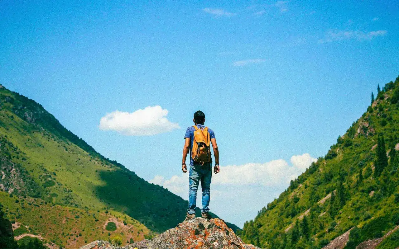 Hombre con mochila en la cima de una roca, disfrutando de un paisaje montañoso ideal para senderismo y trekking.