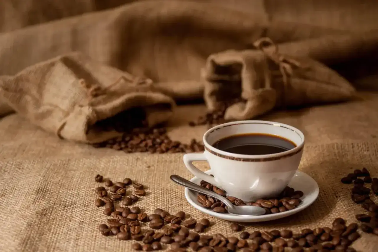 Aromaticzne ziarna kawy rozsypane wokół filiżanki czarnego napoju, jakby przygotowane przez doświadczonego **baristę**.
