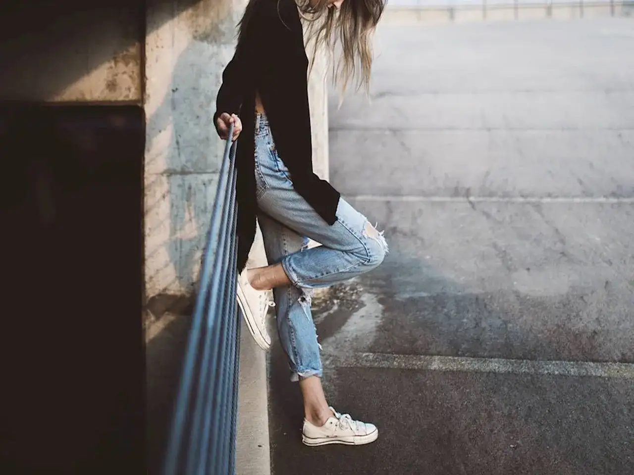 Dziewczyna w luźnych, podartych jeansach i białych trampkach, tworząca modne converse stylizacje damskie.