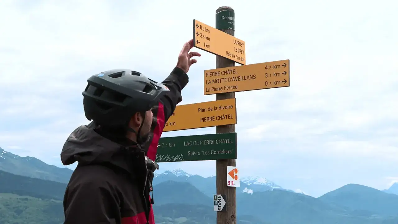 Un randonneur consulte la charte du randonneur, un panneau indicateur avec plusieurs directions et distances, dans un paysage montagneux.