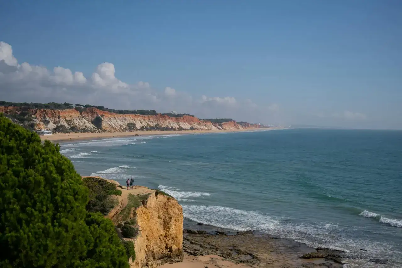 Malownicze wybrzeże Portugalii z klifami, plażą i turkusowym oceanem. Dwie osoby podziwiają widok.