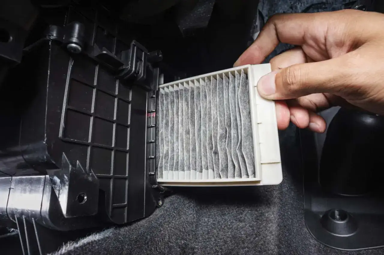 Mano retirando un filtro de aire de cabina sucio. El filtro del aire ¿para qué sirve? Para mantener el aire limpio dentro del coche.