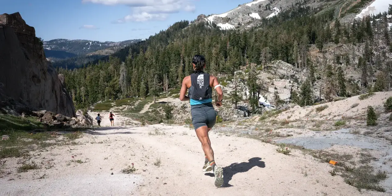 Course de trail en montagne, une femme court sur un sentier rocailleux. La préparation physique est essentielle pour affronter ce terrain exigeant.