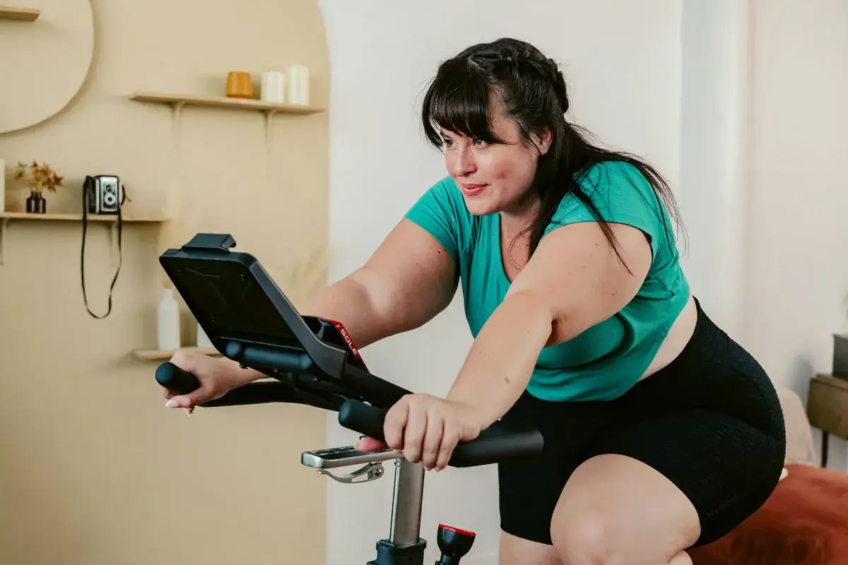 Kobieta ćwiczy na rowerku stacjonarnym. Zastanawiasz się, ile jeździć na rowerku stacjonarnym, by osiągnąć cel?