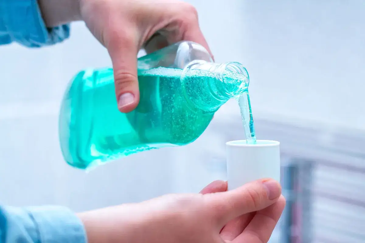Mano vierte l&iacute;quido azul brillante de una botella a una tapa medidora. Es clorhexidina diluida, lista para usar.