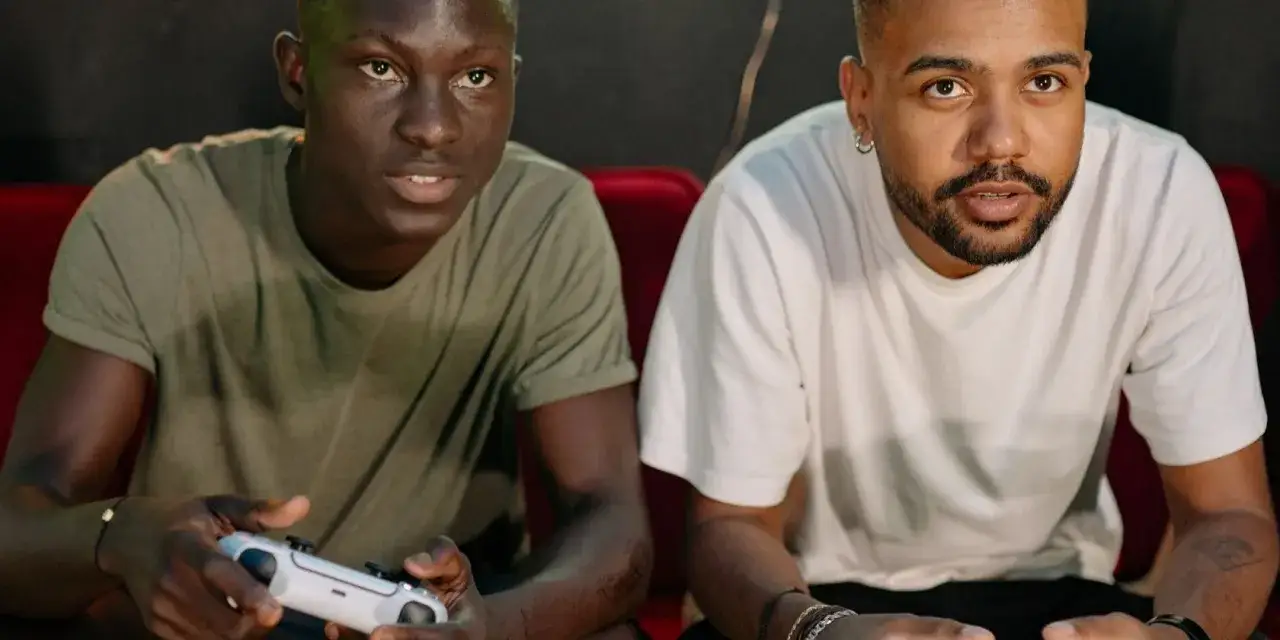 Dwóch przyjaciół gra w gry split screen na Xboxie, jeden trzyma biały kontroler, skupieni na rozgrywce.