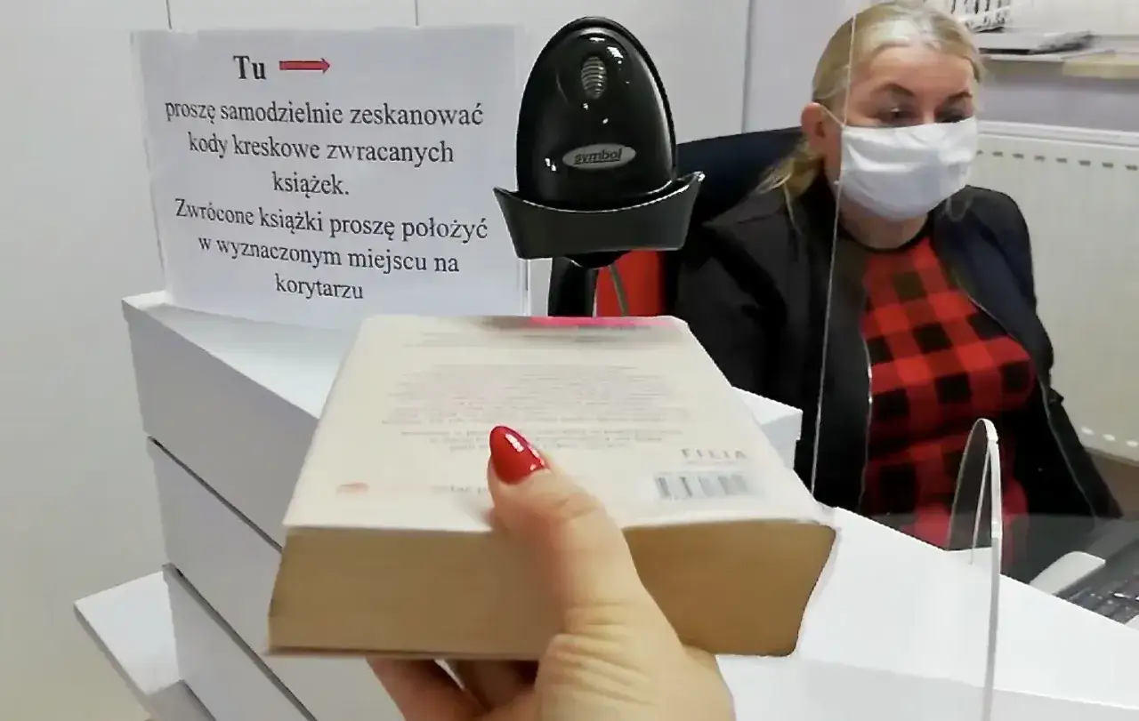 Kobieta w maseczce pracuje w bibliotece, pomagając w zwrocie książek. Nawet bez wykształcenia można tu znaleźć zatrudnienie, obsługując czytelników przy stanowisku samoobsługowym.