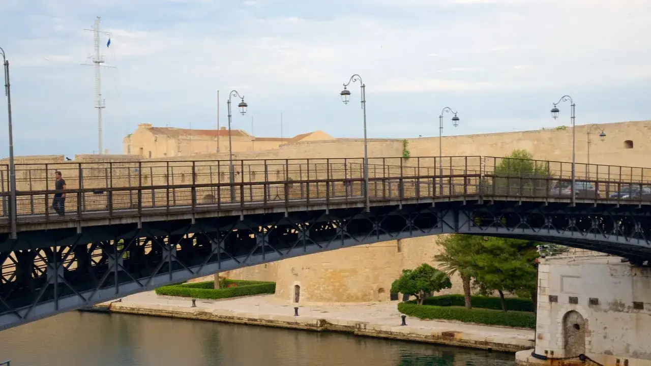Ponte girevole di Taranto, un'idea per cosa vedere a Taranto in mezza giornata. Un uomo cammina sul ponte con la città vecchia sullo sfondo.