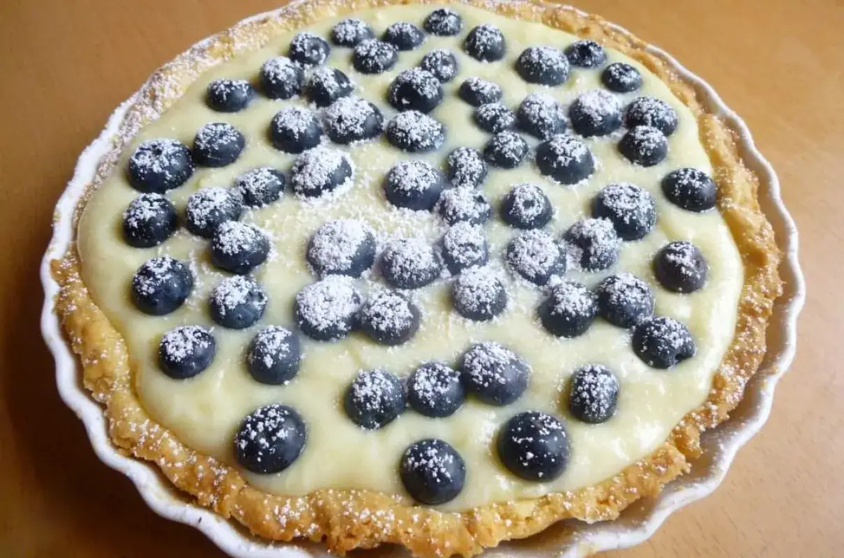 Pyszna tarta z kremem z białej czekolady, udekorowana świeżymi borówkami i posypana cukrem pudrem.