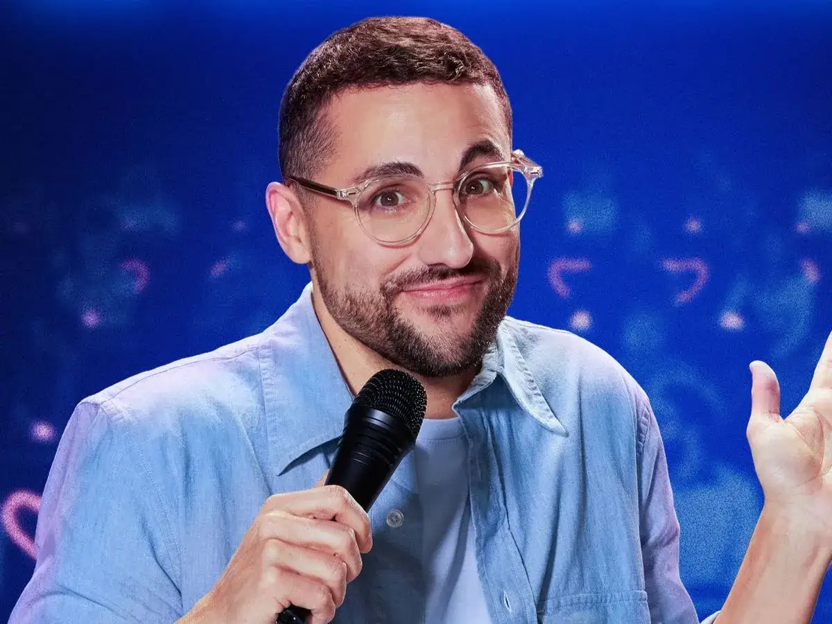 Un cómico con gafas y camisa azul, micrófono en mano, listo para su show en **Galder Varas Madrid**.
