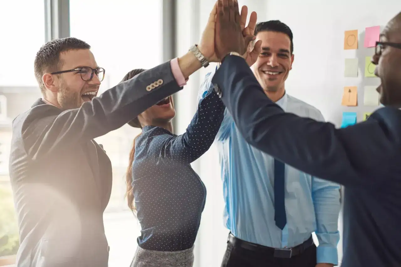 Diverse colleagues high-fiving, smiling, and celebrating success. This image shows what is the foundation for good teamwork: collaboration and shared joy.